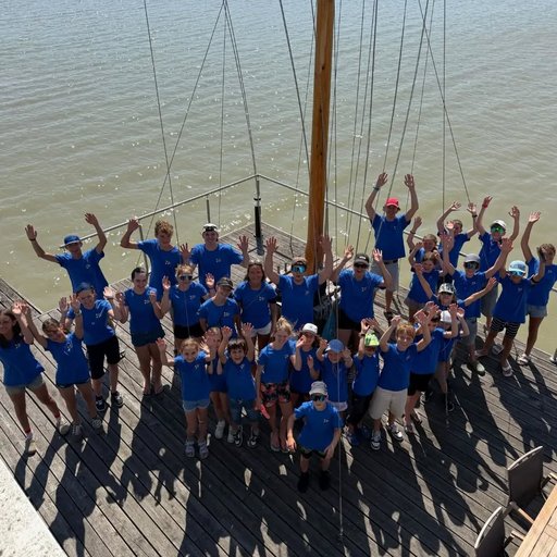 Jugendliche in blauen T-Shirts auf einem Schiff am Wasser heben die Hände