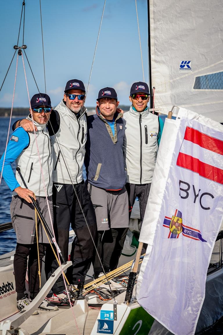 Segel-Team des BYC am Boot mit Fahne vor blauer Kulisse