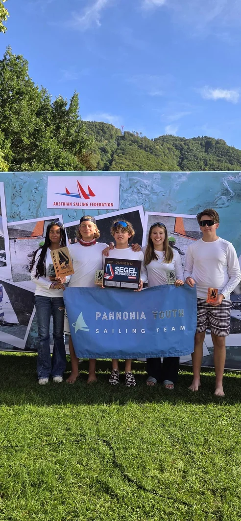 Segel Bundesliga-Sieger mit Pokalen und der Pannonia Youth Sailing Team Fahne vor Bergkulisse